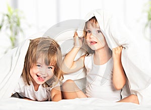 Happy little girls twins sister in bed under the blanket having