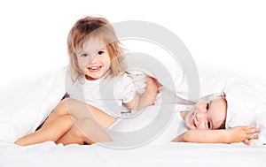 Happy little girls twins sister in bed under the blanket having fun