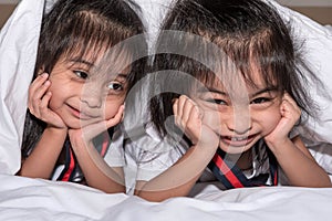 Happy little girls twins sister in bed under the blanket having fun, smiling and wacky