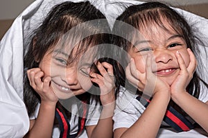 Happy little girls twins sister in bed under the blanket having fun, smiling and wacky