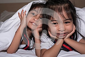 Happy little girls twins sister in bed under the blanket having fun, smiling and wacky