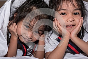 Happy little girls twins sister in bed under the blanket having fun, smiling and wacky