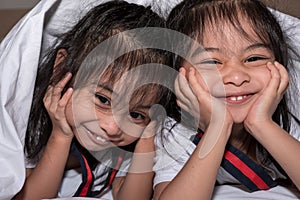 Happy little girls twins sister in bed under the blanket having fun, smiling and wacky