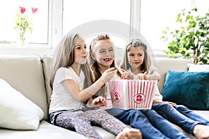 Happy little girls watching comedy movie on tv and eating popcorn at home