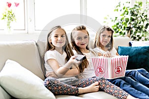 Happy little girls watching comedy movie on tv and eating popcorn at home