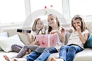 Happy little girls watching comedy movie on tv and eating popcorn at home