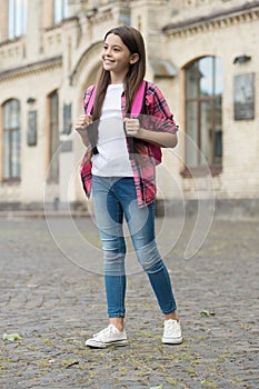Happy little kid back to school in casual style carrying backpack in schoolyard, study