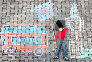 Happy little kid boy in british queen`s guard soldier uniform having fun with London picture drawing with colorful