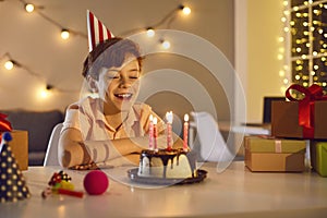 Happy little kid boy celebrating his birthday and blowing candles on homemade baked cake.