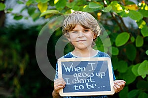 Happy little kid boy with chalk desk in hands. Healthy adorable child outdoors On desk When I grow up I want to be in