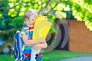 Happy little kid boy in colorful shirt and backpack or satchel and traditional German school bag cone called Schultuete