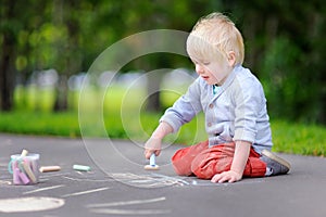 Happy little kid boy drawing with colored chalk on asphalt.