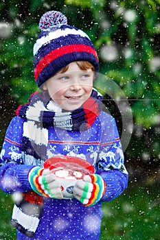 Happy little kid boy drinking hot cocoa and chocolate drink and marshmallows. Funny child in winter sweater, cap, long