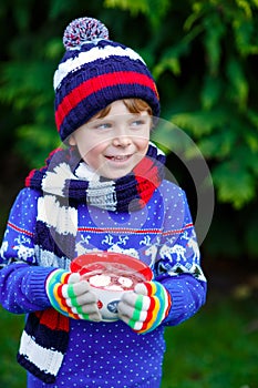 Happy little kid boy drinking hot cocoa and chocolate drink and marshmallows. Funny child in winter sweater, cap, long