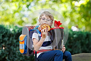 Happy little kid boy with glasses and backpack or satchel on his first day to school . Child outdoors on warm sunny day