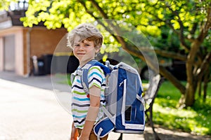 Happy little kid boy with glasses and backpack or satchel on his first day to school or nursery. Child outdoors on warm