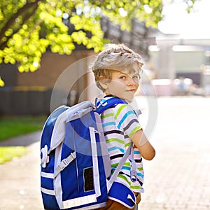 Happy little kid boy with glasses and backpack or satchel on his first day to school or nursery. Child outdoors on warm