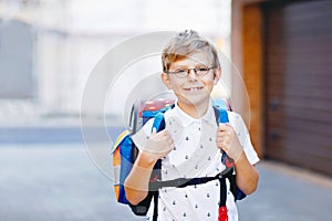 Happy little kid boy with glasses and backpack or satchel. Schoolkid on the way to school. Portrait of healthy adorable