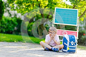 Happy little kid boy with glasses sitting by desk and backpack or satchel