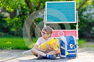 Happy little kid boy with glasses sitting by desk and backpack or satchel