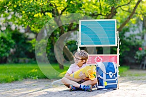 Happy little kid boy with glasses sitting by desk and backpack or satchel