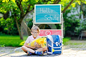 Happy little kid boy with glasses sitting by desk and backpack or satchel. Schoolkid with traditional German school bag