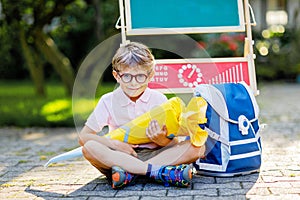 Happy little kid boy with glasses sitting by desk and backpack or satchel. Schoolkid with traditional German school bag