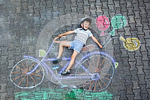 Happy little kid boy having fun with bicycle and air balloons picture drawing with colorful chalks on ground. Children