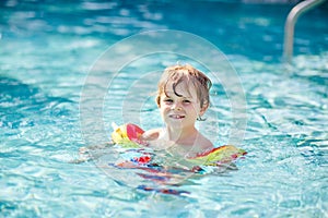 Happy little kid boy having fun in an swimming pool. Active happy child learning to swim. with safe floaties or swimmies