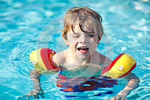 Happy little kid boy having fun in an swimming pool. Active happy preschool child learning to swim. with safe floaties