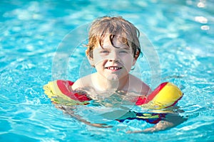 Happy little kid boy having fun in an swimming pool. Active happy preschool child learning to swim. with safe floaties