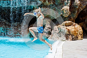 Happy little kid boy jumping in the pool and having fun on family vacations in a hotel resort. Healthy child playing in
