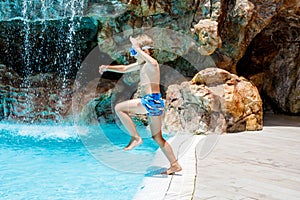 Happy little kid boy jumping in the pool and having fun on family vacations in a hotel resort. Healthy child playing in