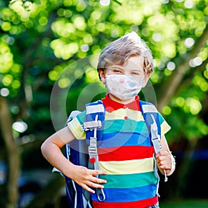 Happy little kid boy, medical mask and backpack or satchel. Schoolkid on way to school. Healthy child outdoors. Back to