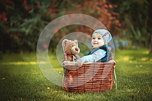 Happy little kid boy playing with bear toy while sitting in basket on green autumn lawn. Children enjoying activity outdoor.