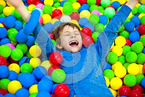 Happy little kid boy playing at colorful plastic balls playground high view. Funny child having fun indoors.