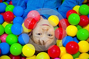 Happy little kid boy playing at colorful plastic balls playground high view. Funny child having fun indoors.