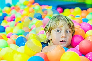 Happy little kid boy playing at colorful plastic balls playground high view. Funny child having fun indoors