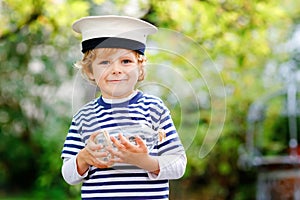 Happy little kid boy in sailor capitain hat and uniform playing with sailor boat ship. Smiling preschool child dreaming