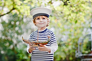 Happy little kid boy in sailor capitain hat and uniform playing with sailor boat ship. Smiling preschool child dreaming