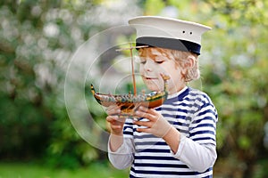 Happy little kid boy in sailor capitain hat and uniform playing with sailor boat ship. Smiling preschool child dreaming