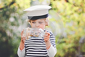 Happy little kid boy in sailor capitain hat and uniform playing with sailor boat ship. Smiling preschool child dreaming