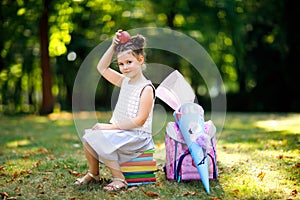 Happy little kid girl with backpack or satchel, books, apple and big school bag or cone traditional in Germany for the