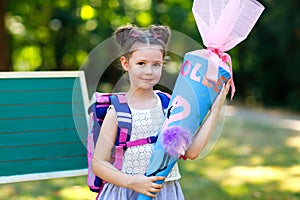 Happy little kid girl by desk with backpack or satchel and big school bag or cone traditional in Germany for the first
