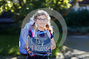 Happy little kid girl with eye glasses with backpack or satchel and big school bag on the first day of school. Healthy