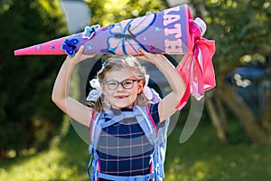 Happy little kid girl with eye glasses with backpack or satchel and big school bag or gift cone traditional in Germany