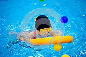 Happy little kid girl learning to swim with pool noodle with coach woman, top view