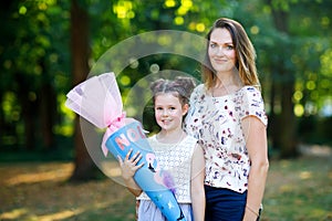 Happy little kid girl and mother with big traditional school gift cone in Germany. schoolkid on first day of elementary