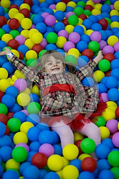 Happy little kid girl in red dress play in pool with colorful plastic balls