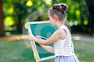 Happy little kid girl standing by big chalk desk Preschool or schoolkid on first day of elementary class. Back to school